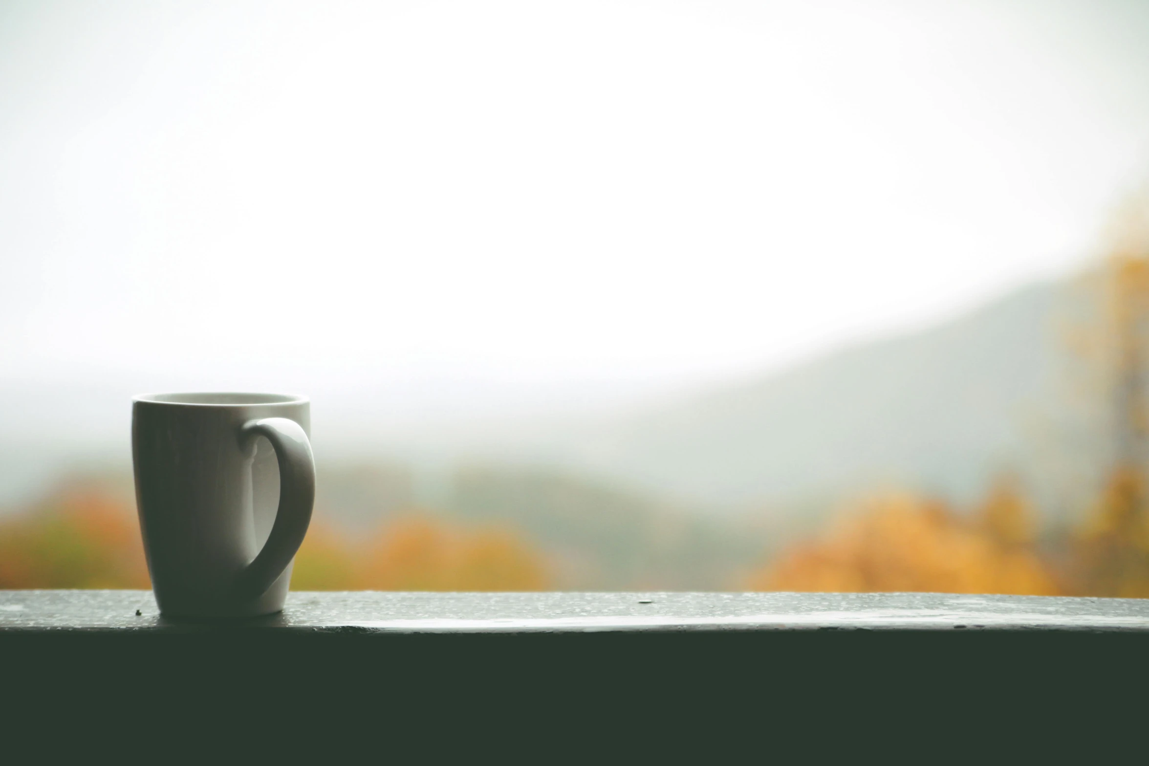 a coffee cup sitting on top of a window sill, pexels contest winner, hills in the background, the fall season, foggy day outside, promo image