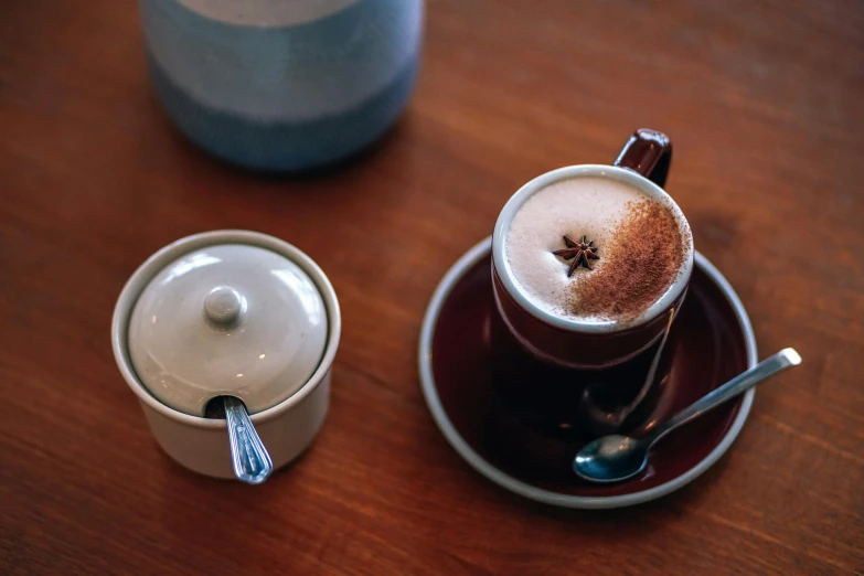 a cup of coffee sitting on top of a saucer, on a wooden table, manuka, red brown and grey color scheme, thumbnail