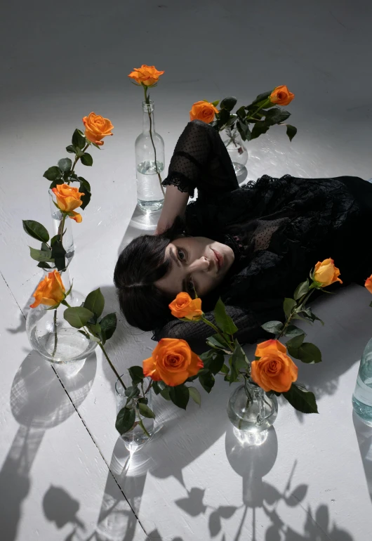 a woman laying on the ground surrounded by flowers, an album cover, unsplash, black and orange, finn wolfhard, laying on roses, elegant floating pose