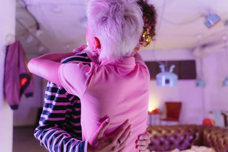 a woman holding a baby in her arms, an album cover, inspired by Nan Goldin, pexels, happening, brightly lit pink room, hugging each other, ninjala, view from back