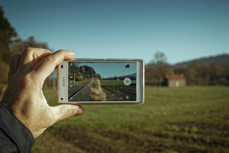 a person taking a picture of a field with a cell phone, a picture, by Thomas Bock, pexels contest winner, photorealism, shot on sony a 7, standing in road, home video footage, old color photograph
