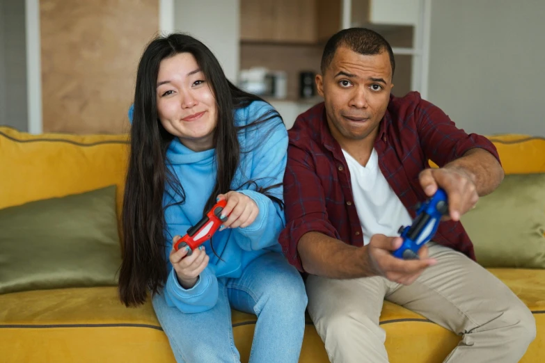 a man and a woman sitting on a couch holding remotes, playing games, red and blue garments, mixed race, promotional image