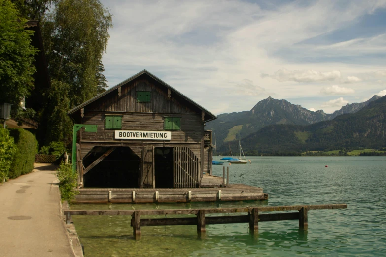 a boathouse sitting on top of a body of water, by Ulrich Leman, pexels contest winner, renaissance, with mountains in background, green waters, programming, brown