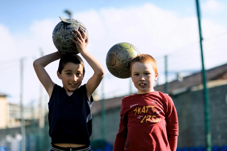 a couple of kids standing next to each other holding a soccer ball, a picture, pexels contest winner, david febland, cone heads, petros and leonid, slightly sunny