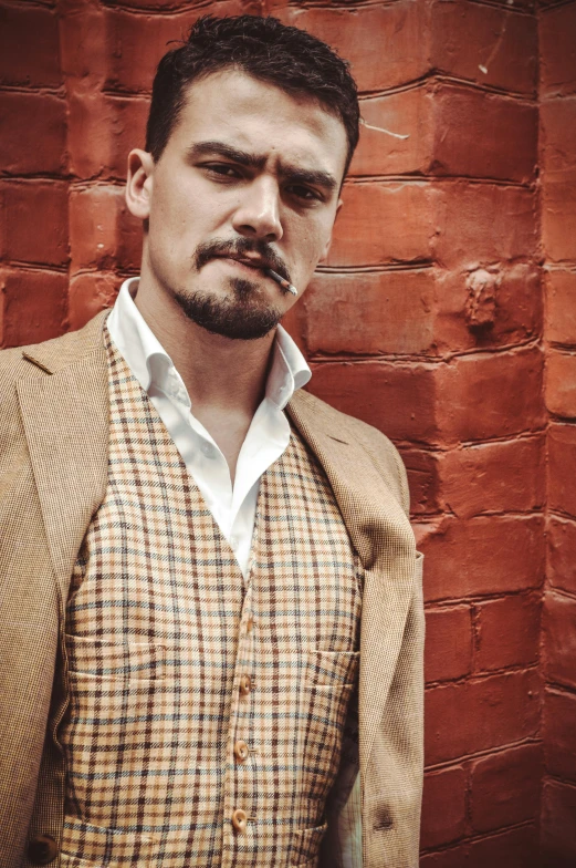 a man standing in front of a brick wall, a portrait, inspired by Ramon Pichot, unsplash, tartan garment, josh brolin, gold waistcoat, wearing a linen shirt