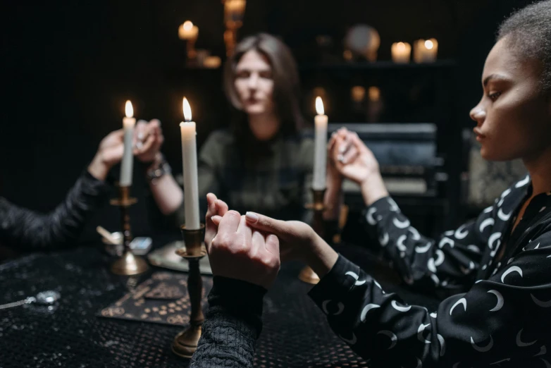 a group of people sitting around a table with candles, doing witchcraft, four hands, 2019 trending photo, fan favorite