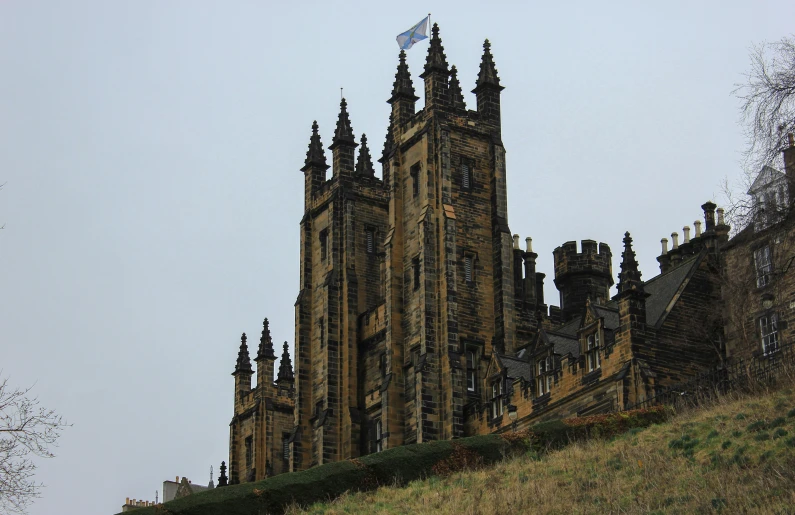 a tall building sitting on top of a lush green hillside, inspired by Dugald Sutherland MacColl, pexels contest winner, art nouveau, outside the'school of magic ', tartan vestments, gothic lighting, wrought iron architecture