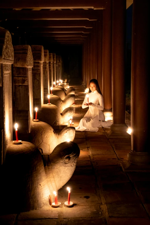 a woman sitting on the ground with candles in front of her, a statue, inspired by Steve McCurry, light and space, in an ancient vault, cambodia, serene lighting, photograph taken in 2 0 2 0