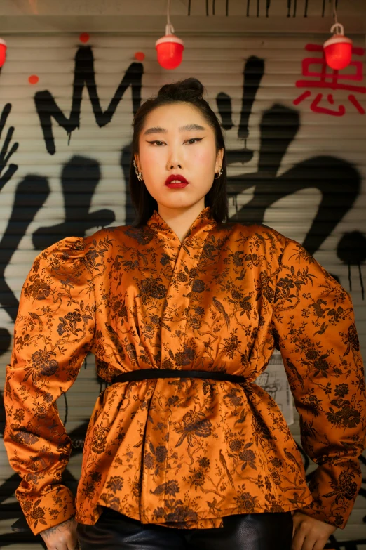 a woman standing in front of a graffiti covered wall, an album cover, inspired by Tang Di, baroque, orange robe, ethnicity : japanese, profile image, street wear