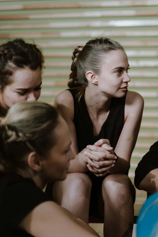 a group of people sitting around a blue ball, prompt young woman, sweaty, deep in thought, sports setting