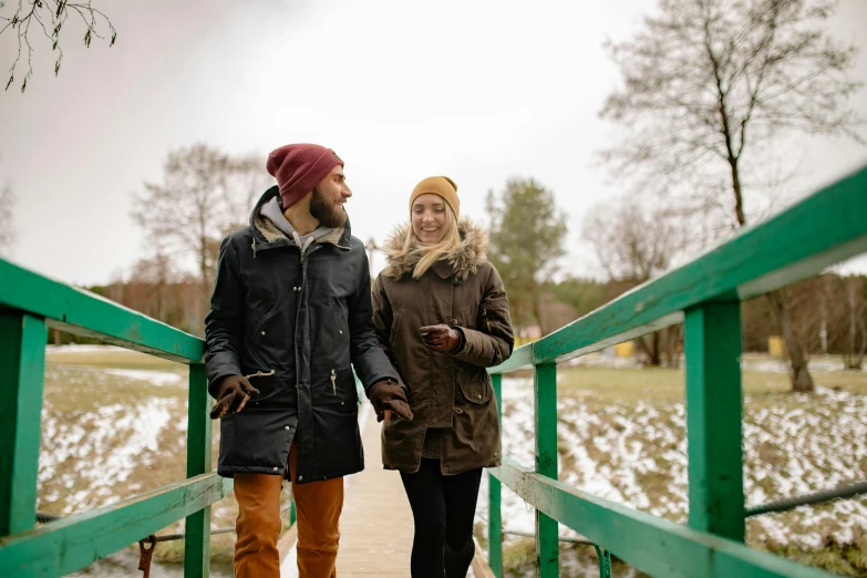 a man and a woman walking across a bridge, by Eero Järnefelt, pexels, wearing teal beanie, smiling couple, a wooden, seasonal