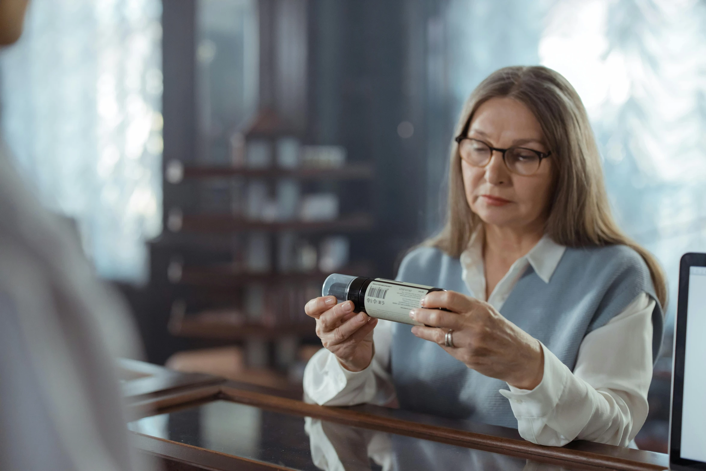 a woman sitting at a desk looking at a cell phone, pexels contest winner, hyperrealism, apothecary, still from half-life movie, graying hair, high quality photo