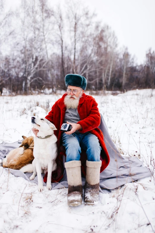 a man sitting on top of a blanket next to two dogs, by Julia Pishtar, pexels contest winner, santa claus, white - haired fox, russian clothes, old cowboy in the arctic