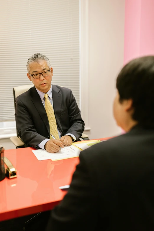 a group of people sitting around a red table, shin hanga, wearing a business suit, working in an office, color photograph, professional profile photo