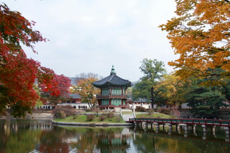 a pagoda sitting on top of a lush green field next to a body of water, inspired by Byeon Sang-byeok, unsplash, autumnal colours, square, traditional korean city, 2000s photo