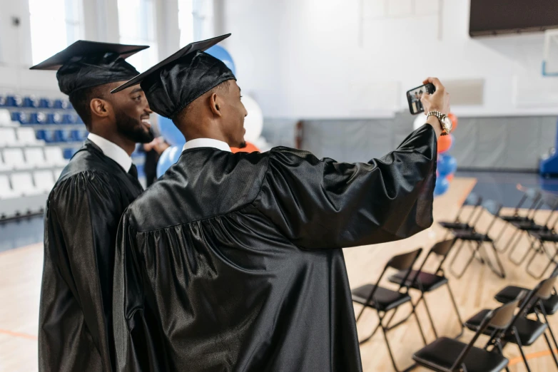 two graduates taking a picture of themselves in their caps and gowns, a picture, shutterstock, black teenage boy, inspect in inventory image, phot, wearing a black robe