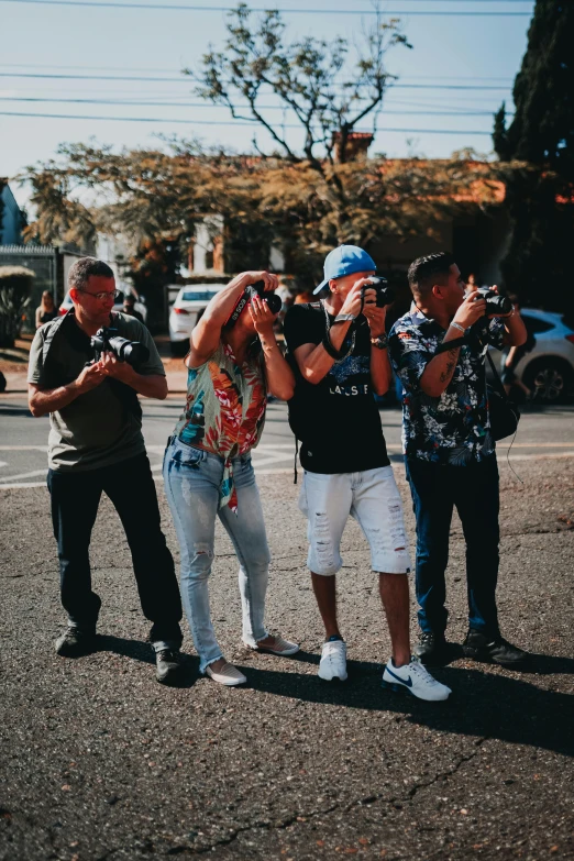 a group of people standing on the side of a road, a picture, by Robbie Trevino, holding a camera, manly, street wear, multicoloured