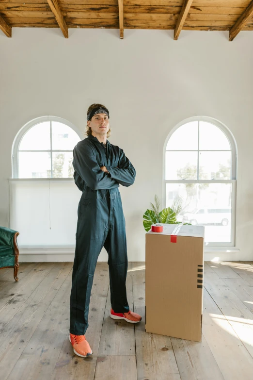 a woman standing in a living room next to a cardboard box, by Nina Hamnett, unsplash, wearing human air force jumpsuit, full body picture of a male monk, confident stance, wearing plumber uniform