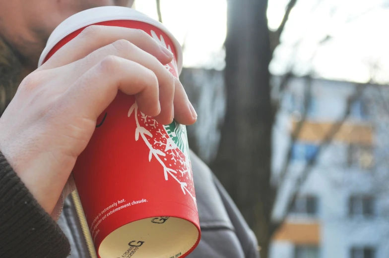 a close up of a person holding a cup of coffee, wearing a red hoodie, starbucks, wearing festive clothing, al fresco