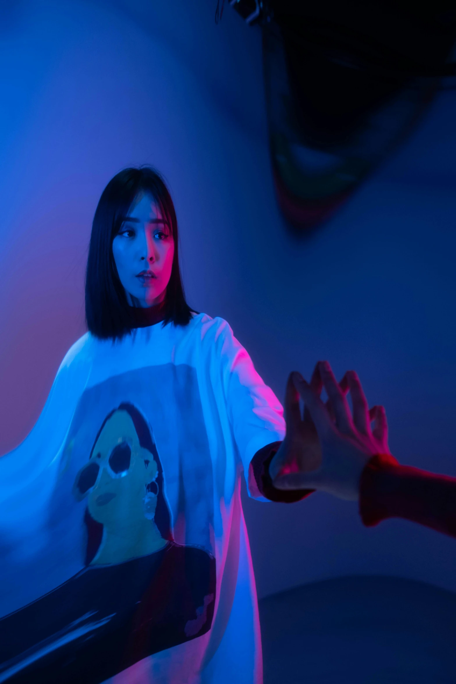 a woman standing in front of a blue light, pexels contest winner, interactive art, wearing a t-shirt, a young asian woman, threatening pose, ( ( theatrical ) )