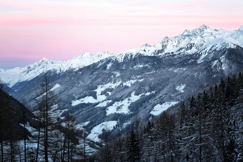 a man riding a snowboard down a snow covered slope, by Peter Churcher, pexels contest winner, romanticism, overlooking a valley with trees, pink hues, early evening, conde nast traveler photo