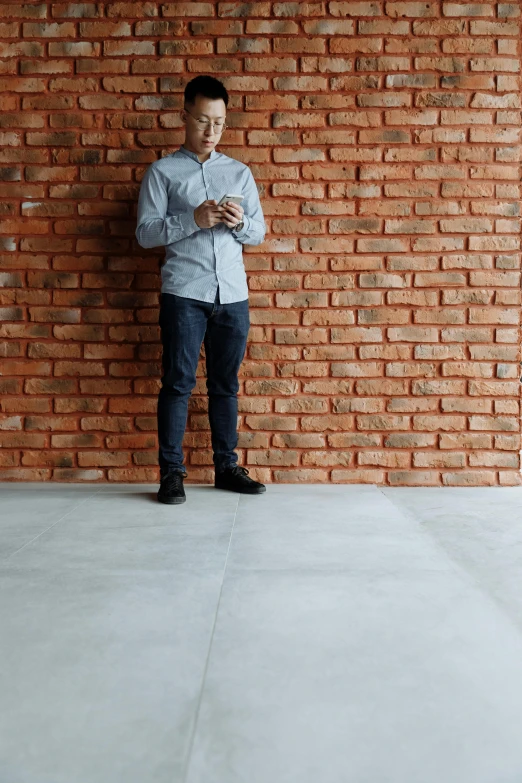 a man standing in front of a brick wall, polished concrete, looking at his phone, floor tiles, profile image