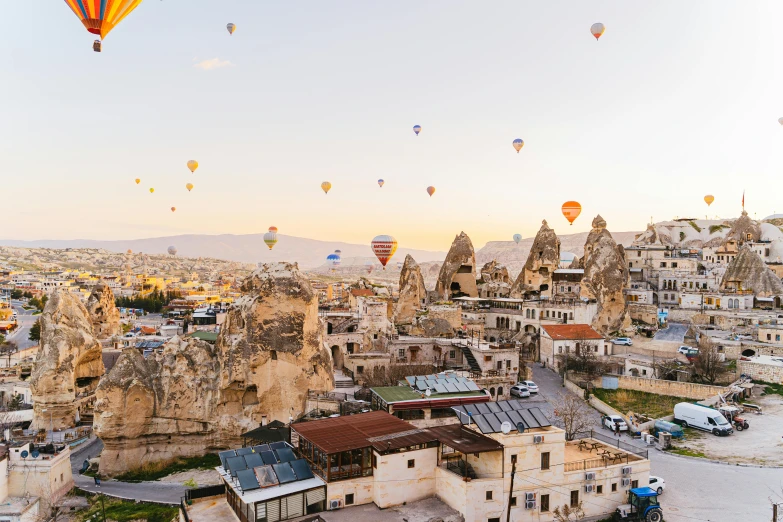 a group of hot air balloons flying over a city, by irakli nadar, pexels contest winner, buildings carved out of stone, overlooking a valley with trees, 🦩🪐🐞👩🏻🦳, turkish and russian