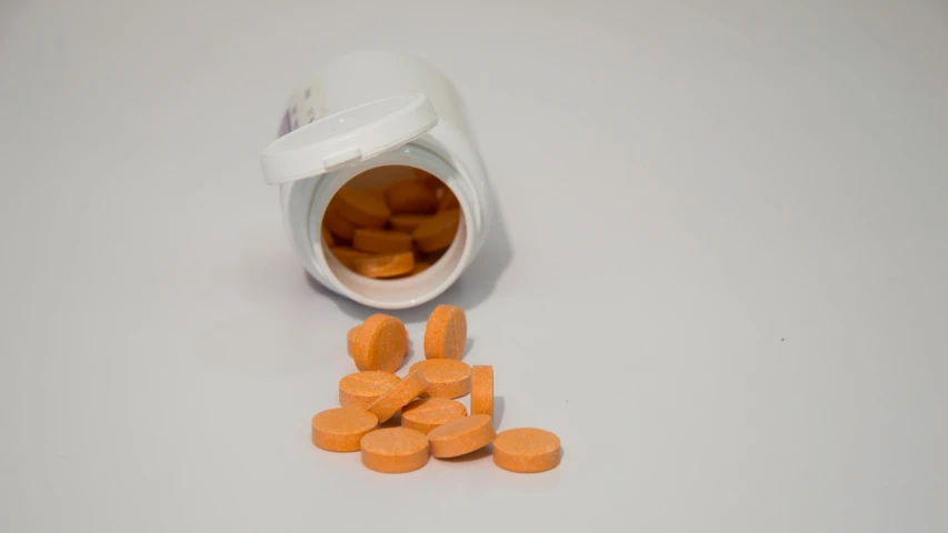a bottle filled with orange pills sitting on top of a table, by Adam Marczyński, pexels, antipodeans, with a white background, cysts, some orange and purple, unedited