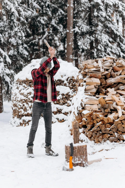 a man standing next to a pile of wood in the snow, inspired by Jakob Häne, pexels contest winner, wearing a flannel shirt, wielding an axe on each hand, 💋 💄 👠 👗, chalet