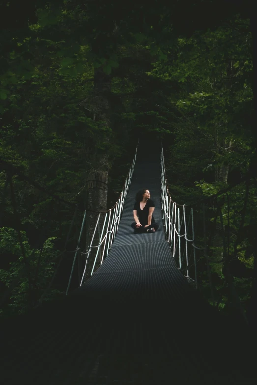 a man sitting on a bridge in the middle of a forest, with a black background, suspended bridge!, 500px photos, new zealand