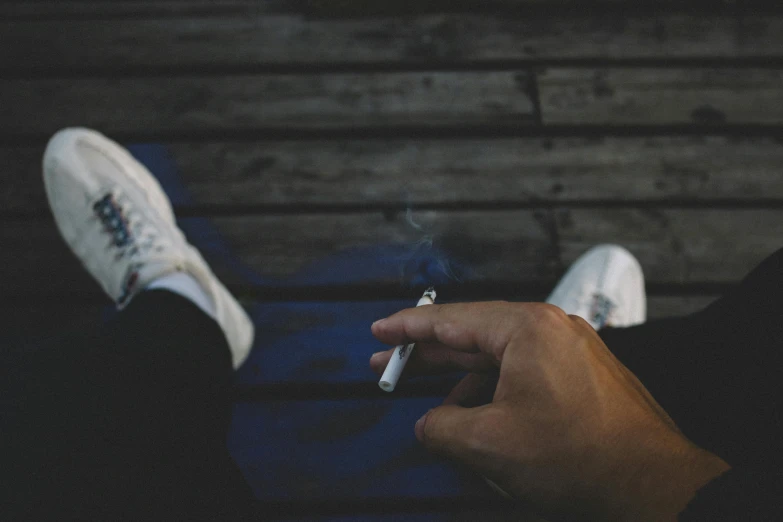 a person sitting on a bench smoking a cigarette, wearing white sneakers, laying on the ground, sitting on man's fingertip, blue and grey