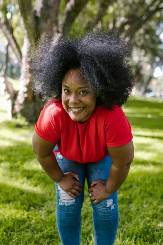 a woman standing on top of a lush green field, natural hair, red shirt, round thighs, at a park