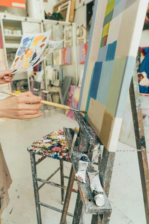 a woman is painting on an easel in a studio, a painting, trending on pexels, arbeitsrat für kunst, feat of artistic achievement, painting on a badge, part petra cortright, accurate portrayal