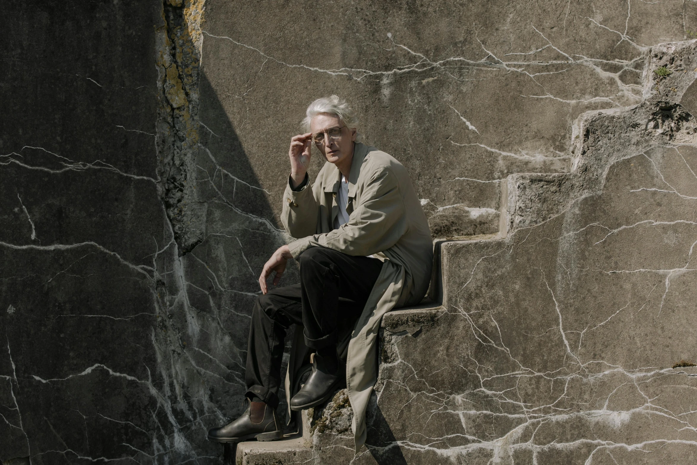 a man sitting on a set of stairs talking on a cell phone, inspired by Carel Willink, unsplash, photorealism, silver haired, geology, ignant, standing over a tomb stone