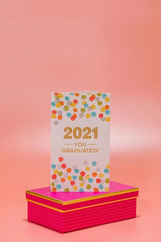 a card sitting on top of a pink box, happening, 2 0 2 1, post graduate, chocolate candy bar packaging, yo )