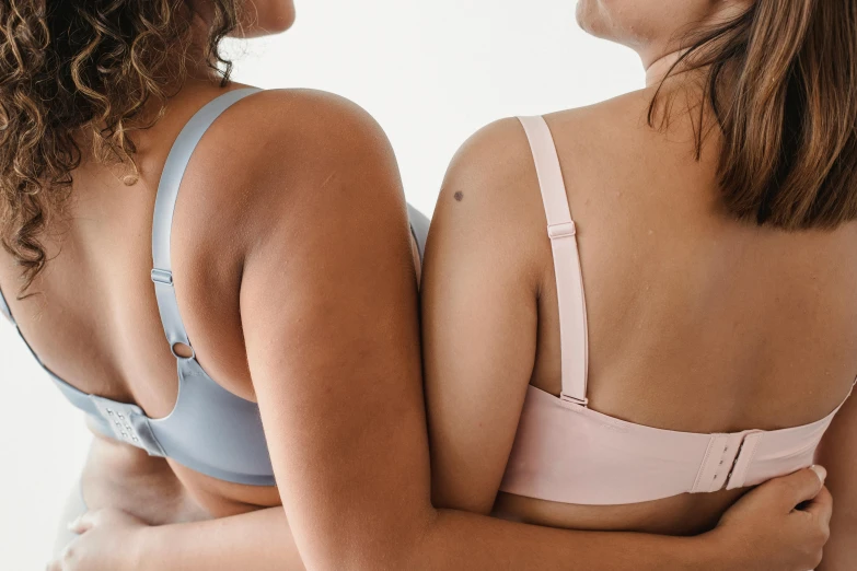 a couple of women standing next to each other, unsplash, posing together in bra, muted colours, showing her shoulder from back, bottom body close up