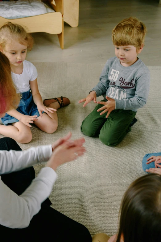 a group of children sitting on the floor in a circle, hands reaching for her, talking, thumbnail, digital still