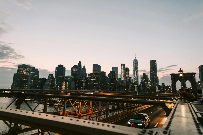 a car driving across a bridge with a city in the background, pexels contest winner, happening, new york buildings, summer evening, rooftop romantic, ultrawide lens”