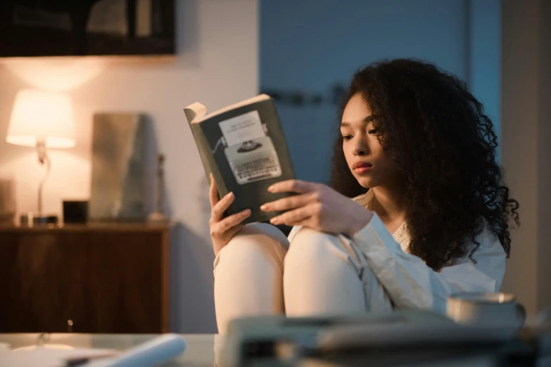 a woman sitting on a couch reading a book, pexels contest winner, renaissance, tessa thompson, lighting her with a rim light, sitting on edge of bed, reading engineering book