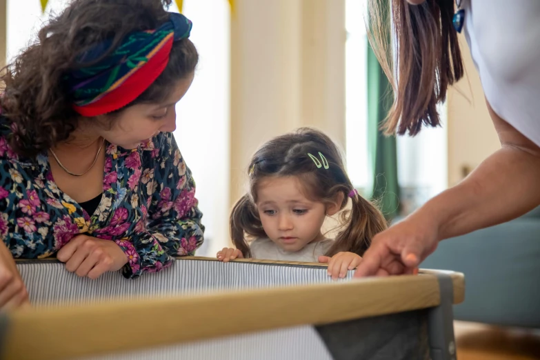 a woman helping a little girl with a loom, by Arabella Rankin, interactive art, high angle close up shot, 3 sisters look into the mirror, in a classroom, low quality photo