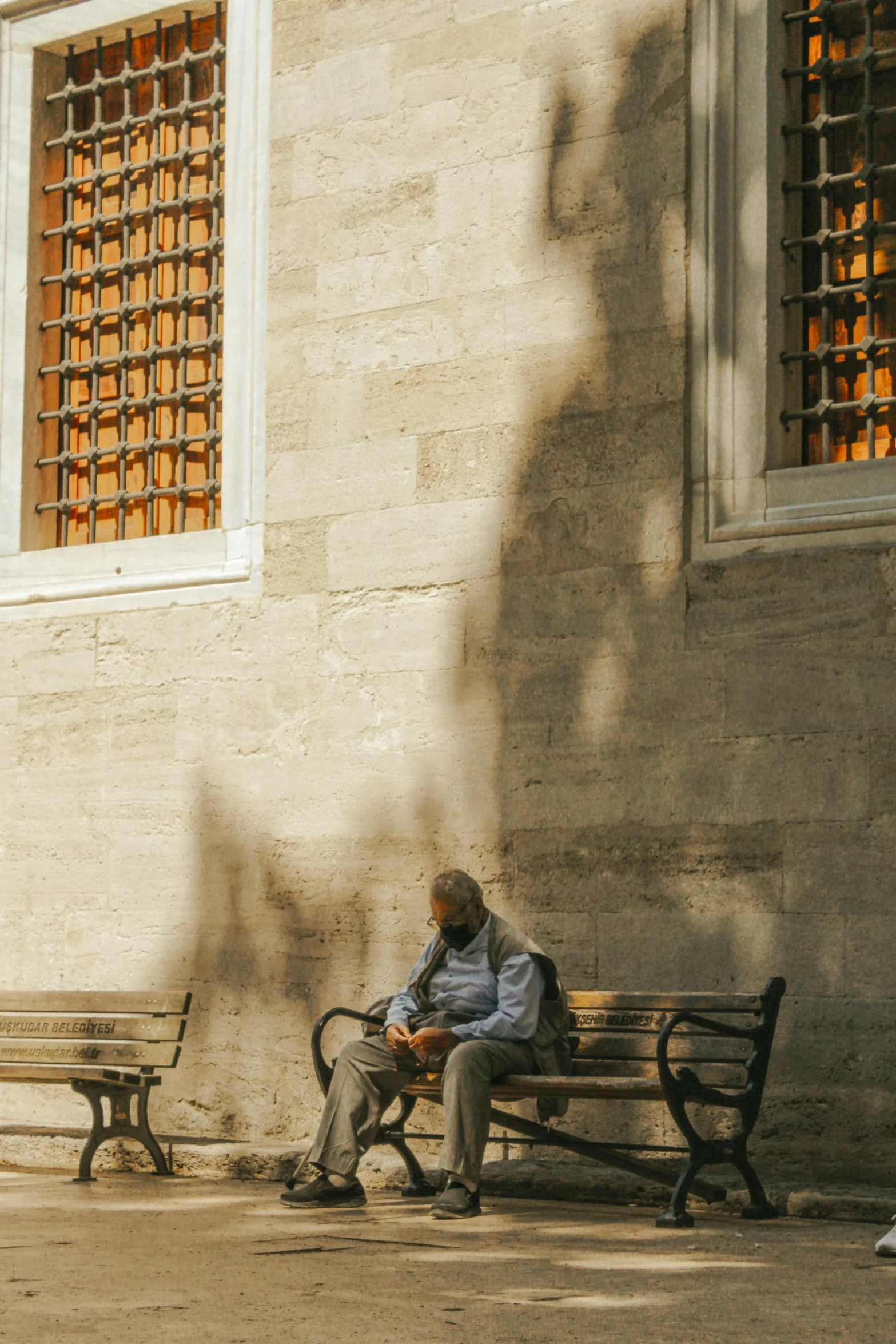 a man sitting on a bench in front of a building, a picture, inspired by Altoon Sultan, pexels contest winner, neoclassicism, dappled afternoon sunlight, today\'s featured photograph 4k, brown, turkey