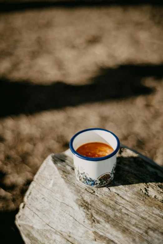 a cup of coffee sitting on top of a wooden table, holding hot sauce, cliffside, detailed product image, low sun