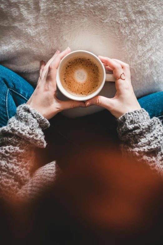 a person holding a cup of coffee in their hands, trending on pexels, sitting with wrists together, hugging, instagram post, full-figure