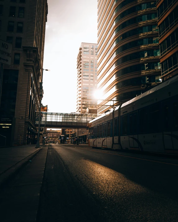 a train traveling down a city street next to tall buildings, unsplash contest winner, light and space, sunshafts, downtown, morning light showing injuries, architecture photo