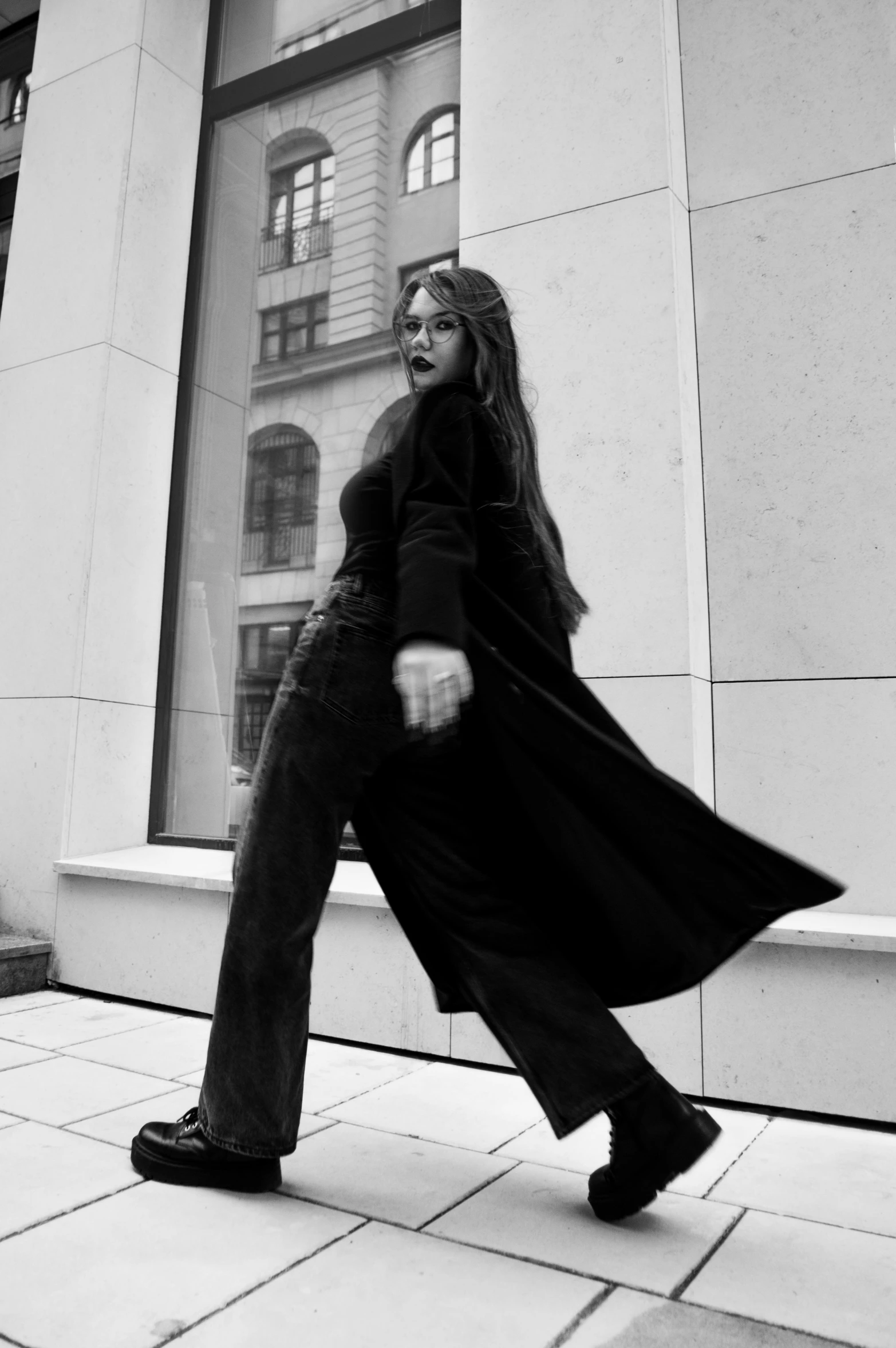 a black and white photo of a woman walking down a sidewalk, a black and white photo, unsplash, realism, ariana grande as a sith, doing a sassy pose, longcoat, nyc