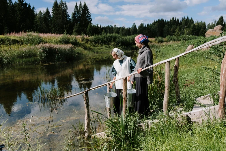 a couple of people standing next to a body of water, hurufiyya, midsummer, older woman, in the countryside, documentary photo