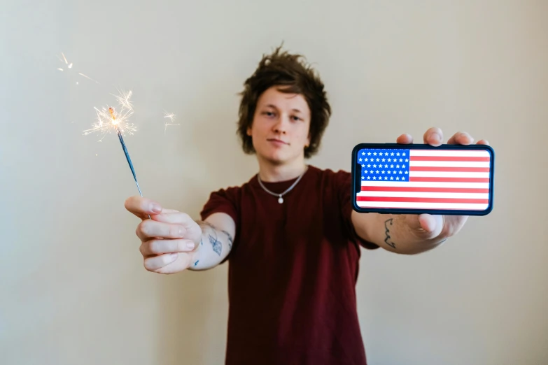 a man holding a sparkler and a cell phone, an album cover, pexels, american realism, flag in his right hand, telegram sticker, connor hibbs, adafruit