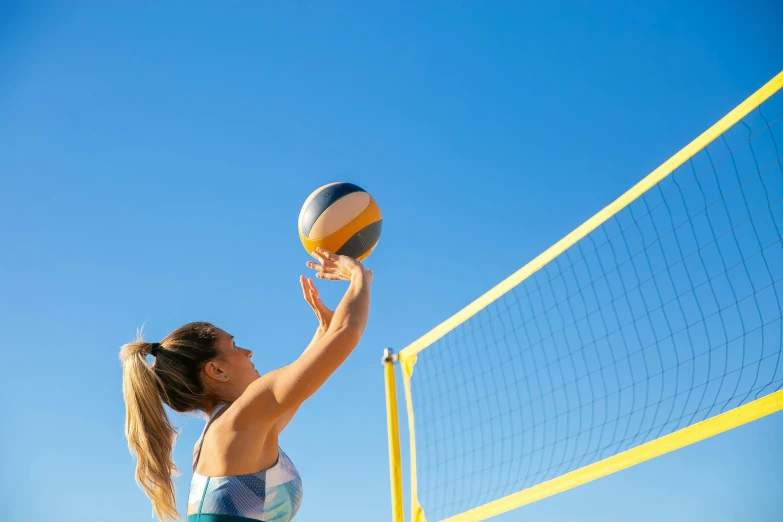 a woman reaching up to hit a volleyball ball, arabesque, clear blue skies, profile image, in a beachfront environment, vibrant colour