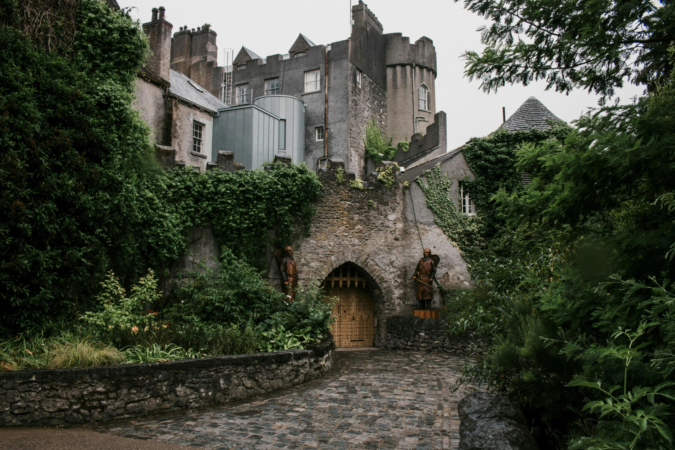 a castle sitting on top of a lush green hillside, unsplash, art nouveau, brutalist courtyard, entrance, cosy, grey