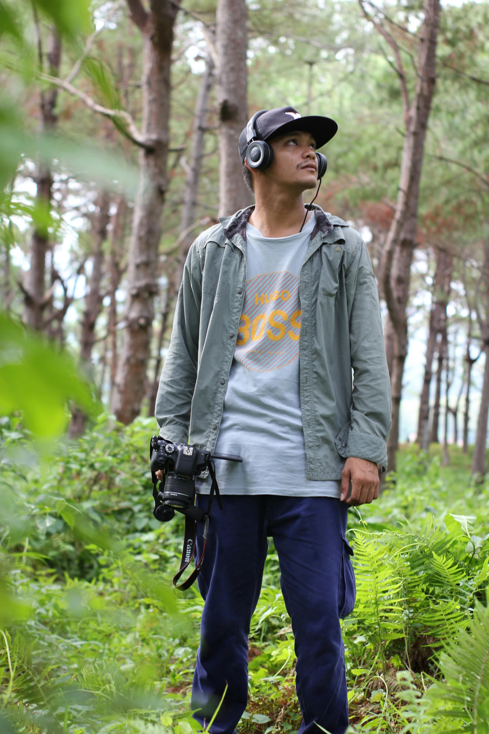 a man standing in the woods with a camera, inspired by Rudy Siswanto, happening, grey hoodie, in tshirt, with head phones, cinematic. ”